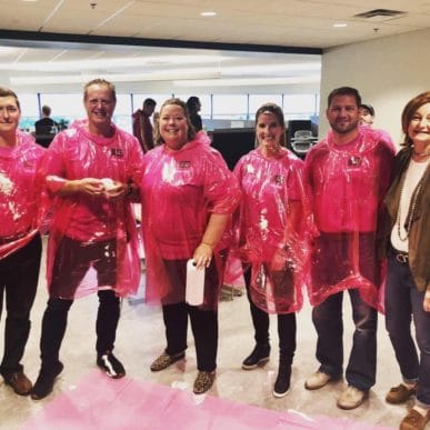 Attane's Executive Leadership team wearing pink ponchos as they prepare to be pied in the face to raise money for Breast Cancer Awareness