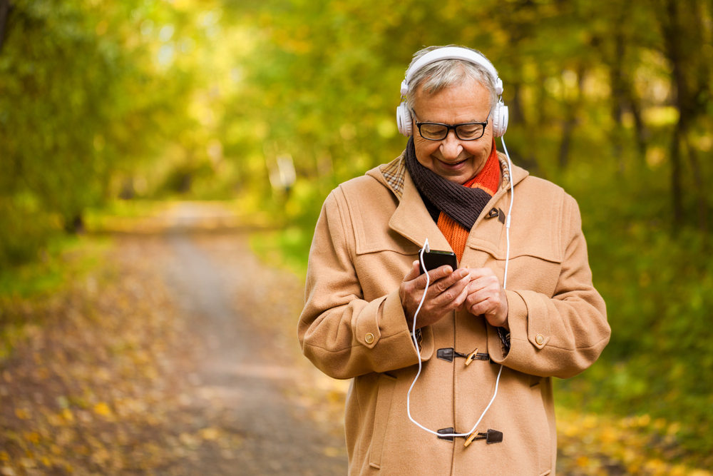Senior man bundled up for a late autumn walk listens to a podcast on his phone