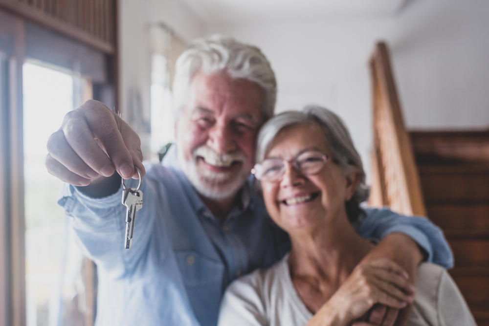 An older man and an older woman proudly show off the keys to a house
